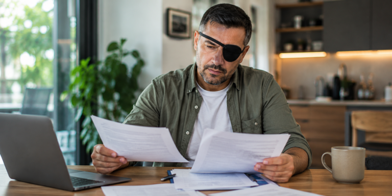 Homem com visão monocular revisando documentos previdenciários em casa.